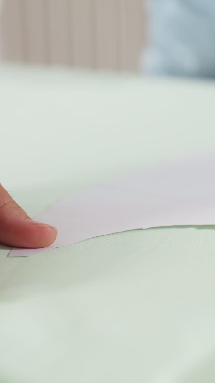 Hands smooth fabric, Assistant flattens cloth with care, Preparing layout by aligning fabric and paper, Closeup of hands ensuring fabric smoothness and precise paper positioning during preparation