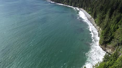 aerial view of grey sand mystic beach and green conifer forest on vancouver island coastline, scenic landscape on sunny day, drone shot