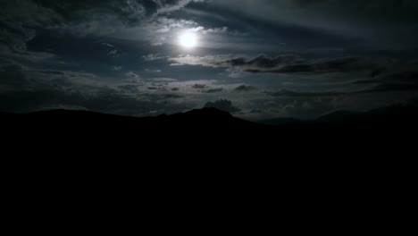 Hiperlapso-De-Luna-Llena-En-Una-Noche-Nublada-Con-Silueta-Oscura-De-Montañas