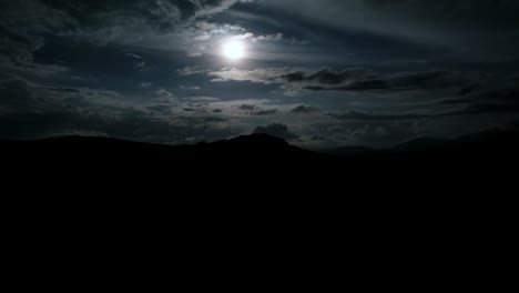 hiperlapso de luna llena en una noche nublada con silueta oscura de montañas