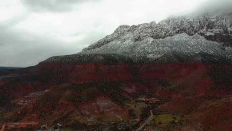 aerial push in shot showcasing the vivid red rock mountains during a snow fall.