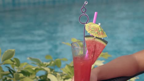 girl-holds-tall-glass-in-hand-against-blue-swimming-pool