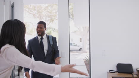 woman opens front door of house and hugs business husband returning home from work