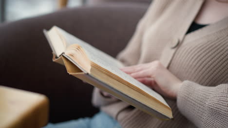 close-up of young lady seated comfortably flipping through pages of her book, engaging in reading. she turns to next page while immersed in content