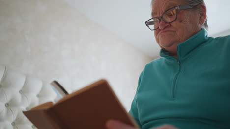 elderly woman reading book with magnifying glass, holding it close to her face. she appears focused on the text, showcasing a serious expression while trying to read small print in a cozy indoor setting