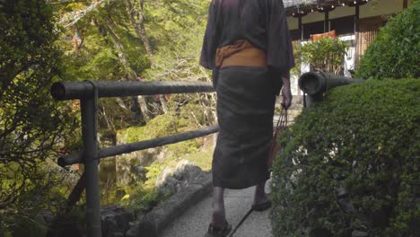 Slide-shot-of-a-person-wearing-a-Hakama-walking-over-a-bridge-in-a-Japanese-garden-in-Kyoto,-Japan-4K-slow-motion