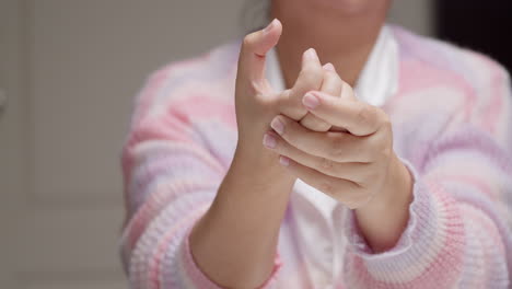 a lady wearing a pink and purple stripes sweater is pinching her hand knuckles and fingers, while massaging herself to relieve them of inflammation and pain