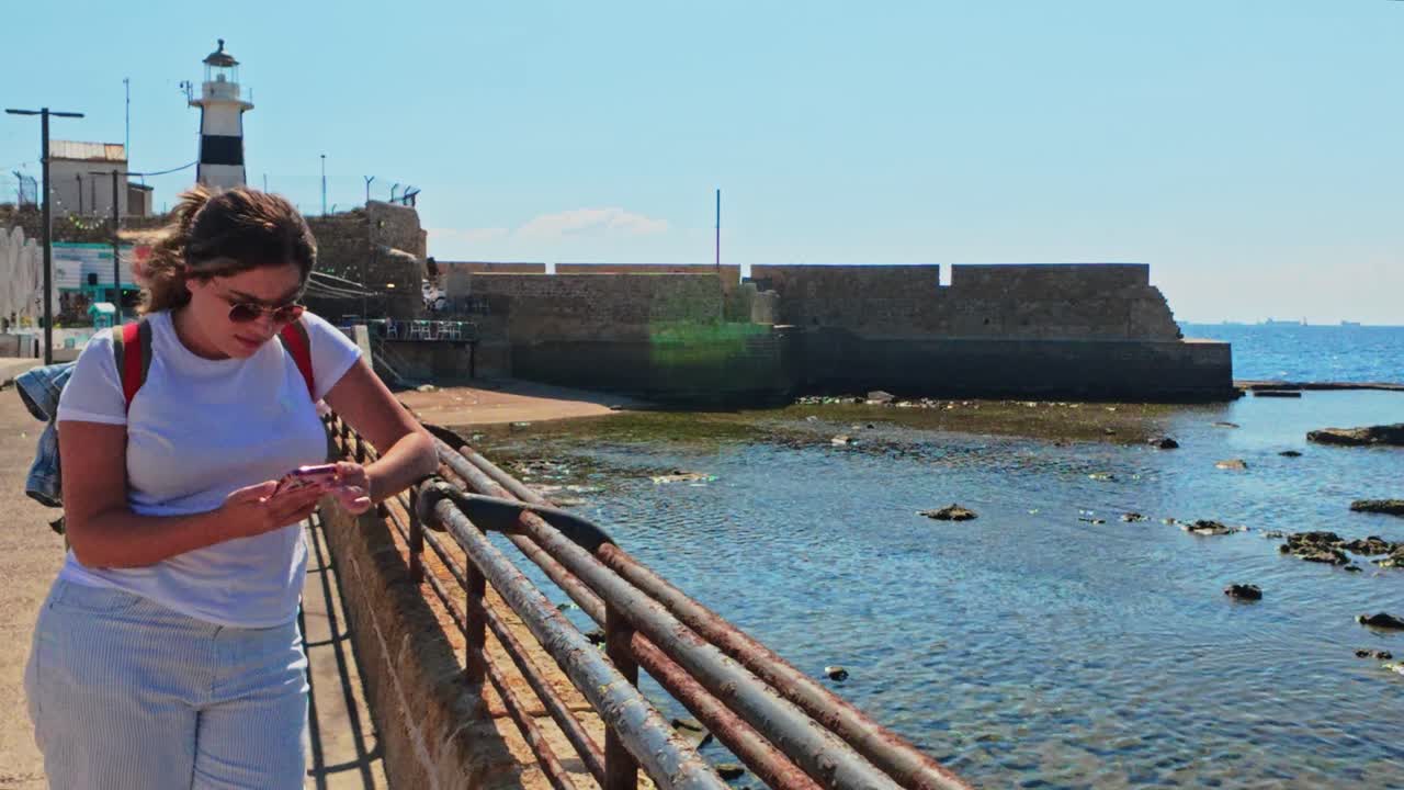 Tourist girl using mobile phone by the sea in Old City Akko