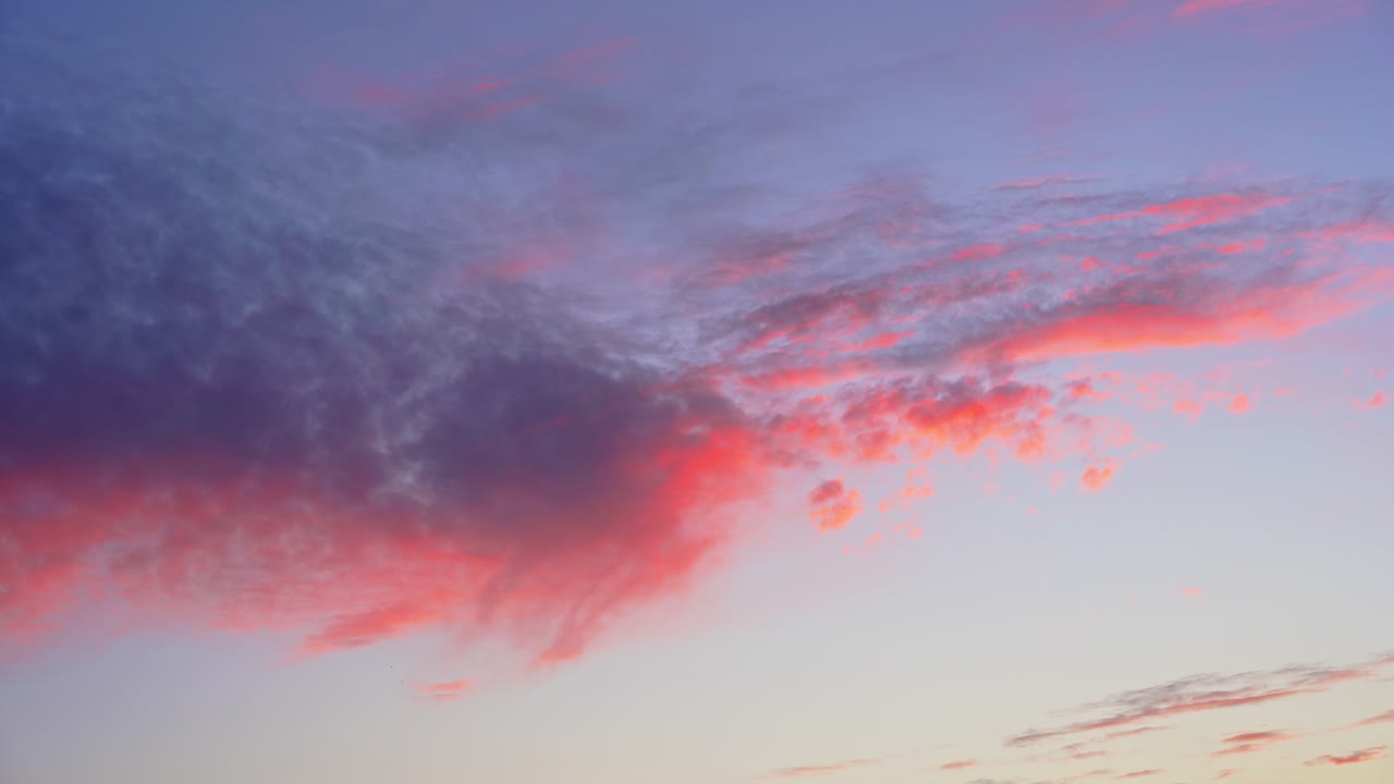 Nuvole colorate rosa e blu al tramonto che fluttuano in un cielo serale aperto, creando uno sfondo atmosferico delicato con vivaci tonalità crepuscolari e una luce naturale drammatica