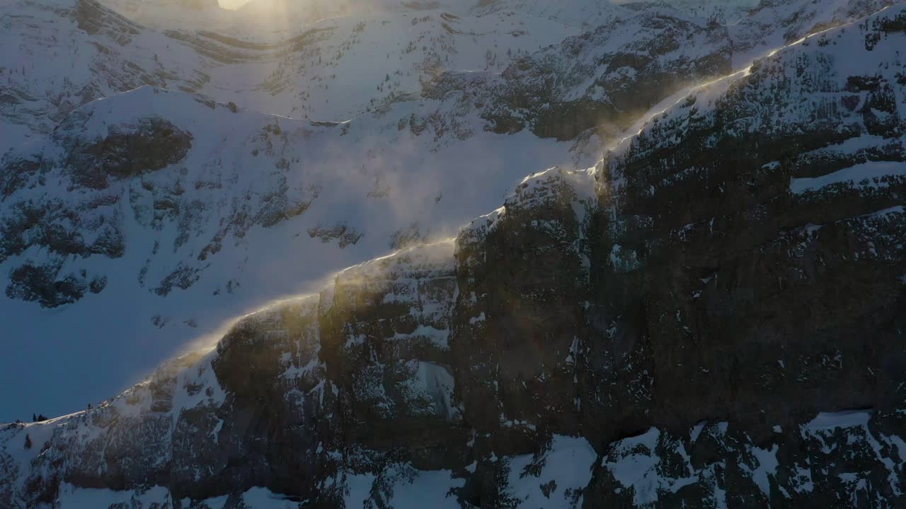 Avvicinamento con drone al tramonto di neve scintillante che soffia via dalla cresta della montagna