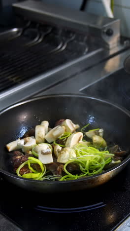cooking food in frying pans. chef pouring sauce into the frying mushrooms. making fried mixed vegetable with sauce in metal pan in the restaurant kitchen. vertical video
