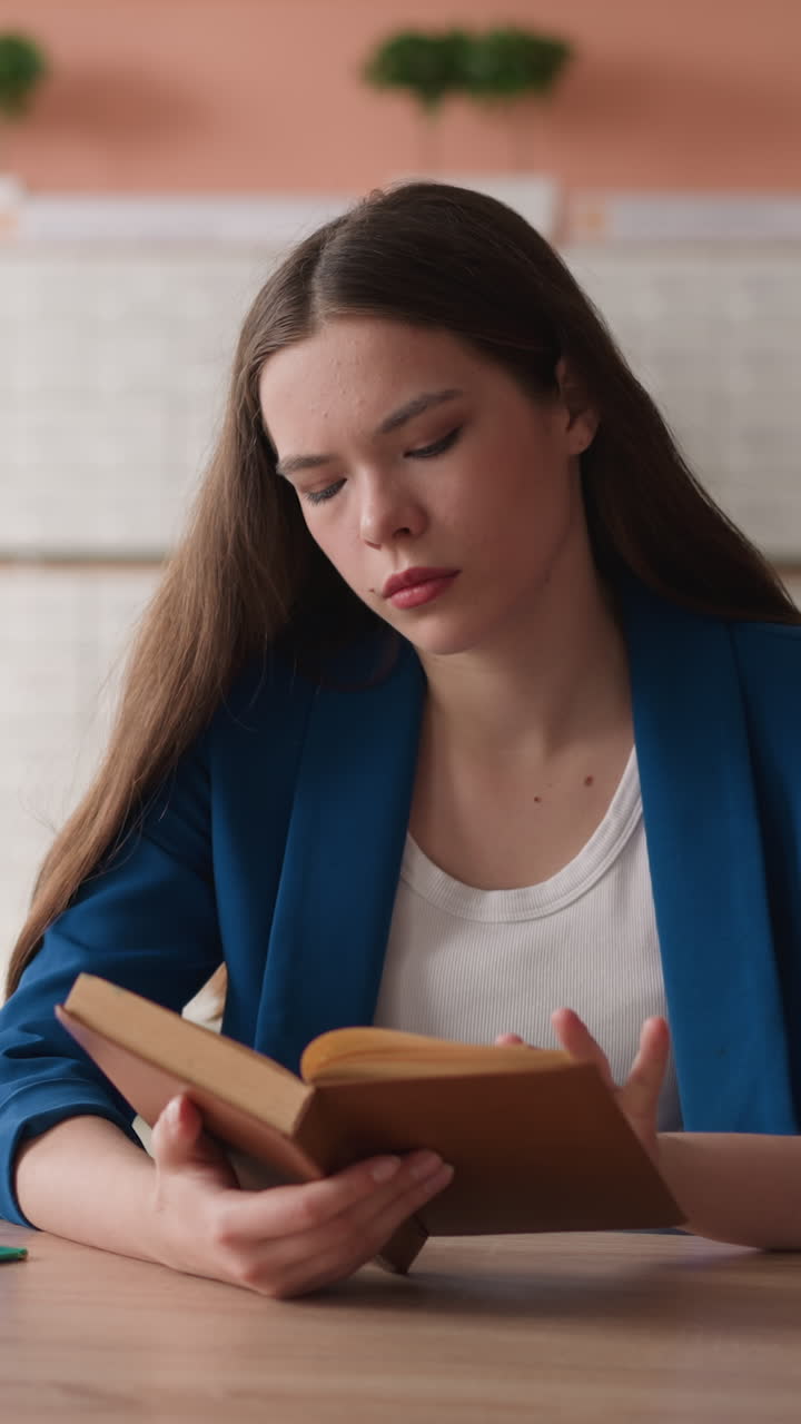 Woman turns page of book sitting at desk in library. Young woman learns literature preparing for exam in college library. Graduate prepares for final test