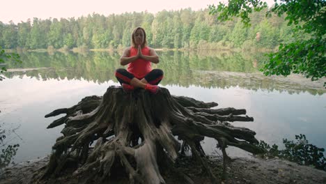 a caucasian woman in sportswear sitting on a tree stump and practicing yoga