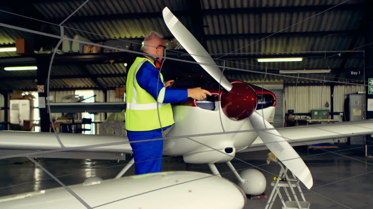 Senior mechanic inspecting cowling inside hangar, showing floating aviation icons and data graphs