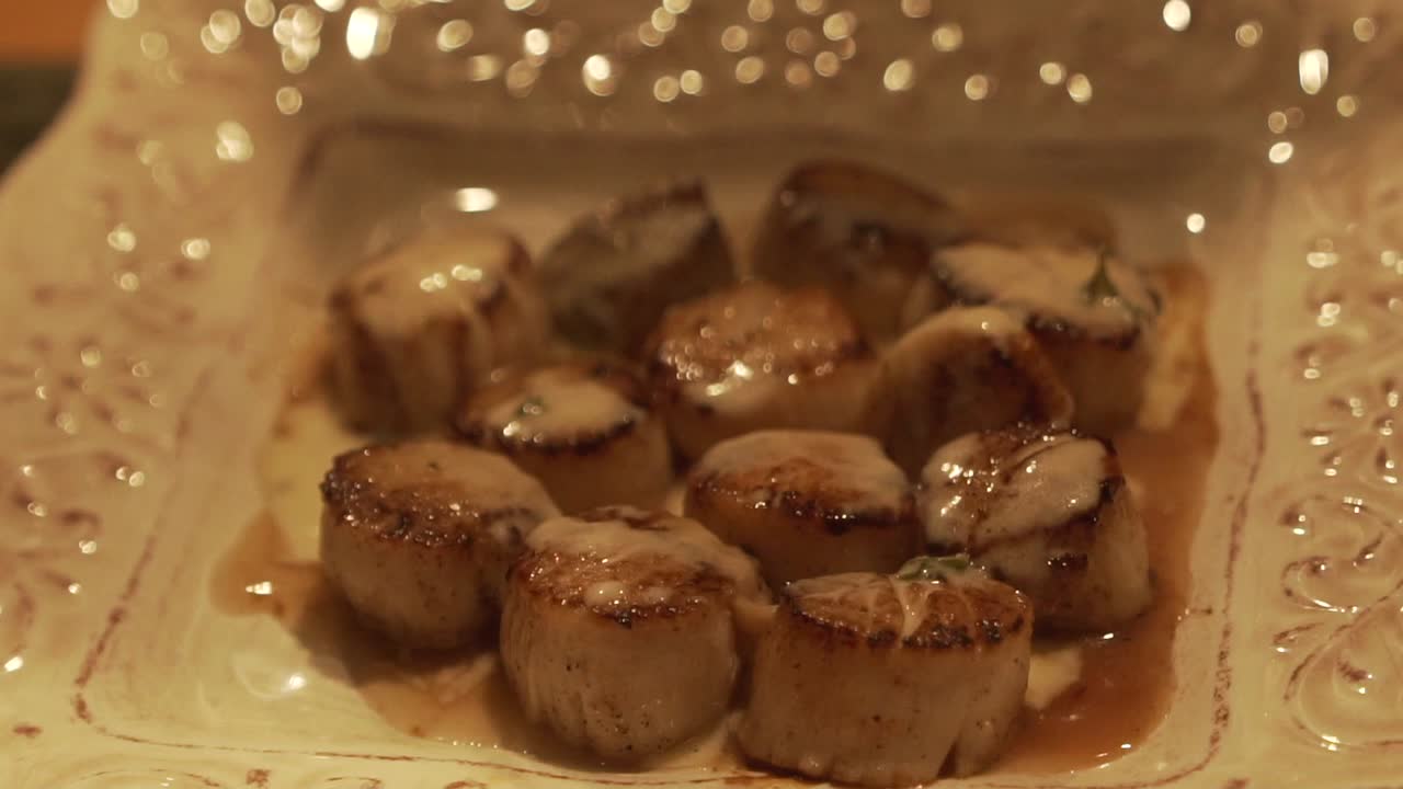 Slow motion static shot of grilled sea scallops being drizzled with white sauce in HD 1080p 23.98p