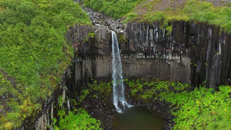 svarti foss fluyendo sobre columnas de basalto en el parque nacional skaftafell en la costa sur de islandia - retroceso aéreo