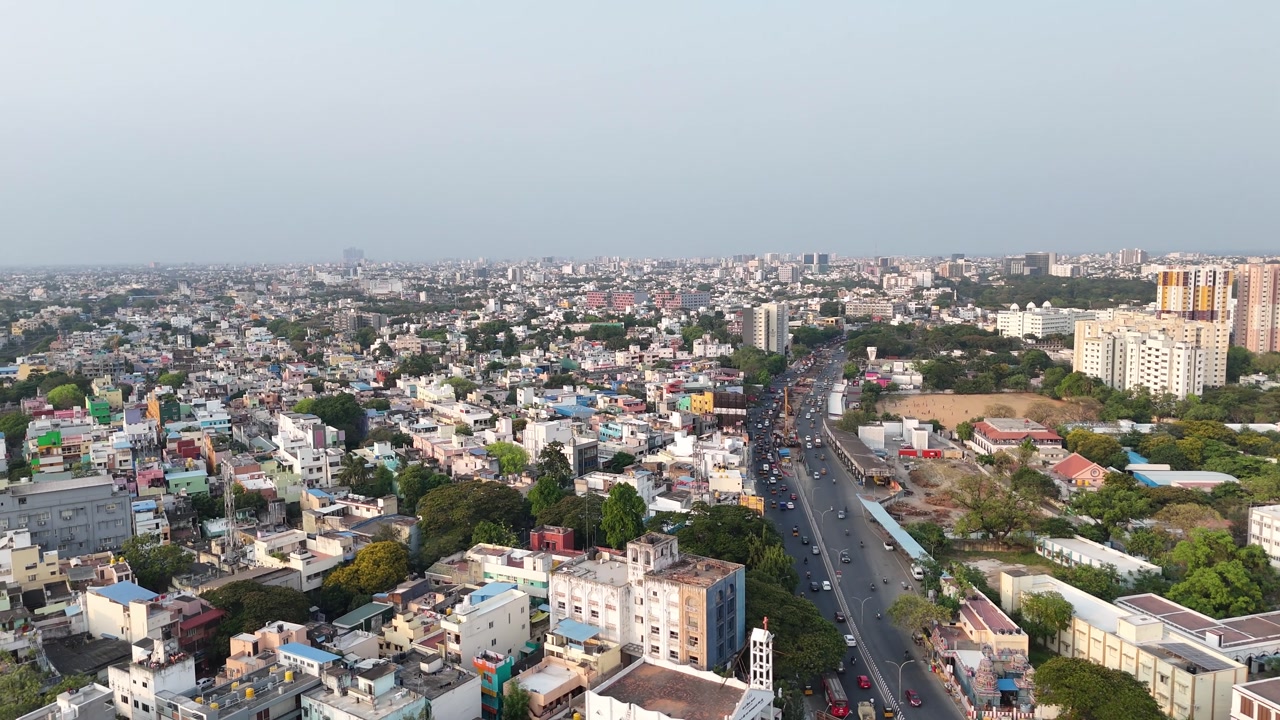 Chennai's busy Anna Salai, Saidapet. Traffic fills the central road, flanked by a lively field on the left and commercial structures on the right. A distant elevated flyover