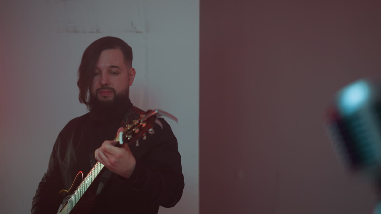 un guitarrista barbudo con un traje negro toca la guitarra contra un fondo blanco. el enfoque está en su expresión enfocada y su habilidad en tocar
