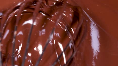 a whisk gently stirs through smooth, glossy melted chocolate, creating rich textures and reflections.