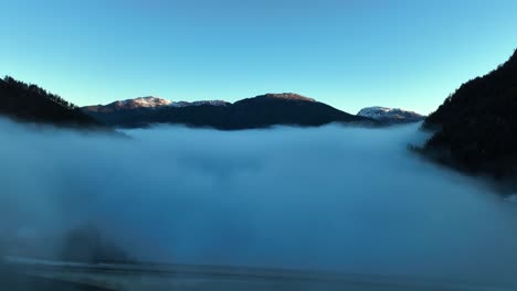 Kallestadsundet-bridge-and-Norway-mountains-seen-above-morning-haze,-Blue-sky-morning-aerial