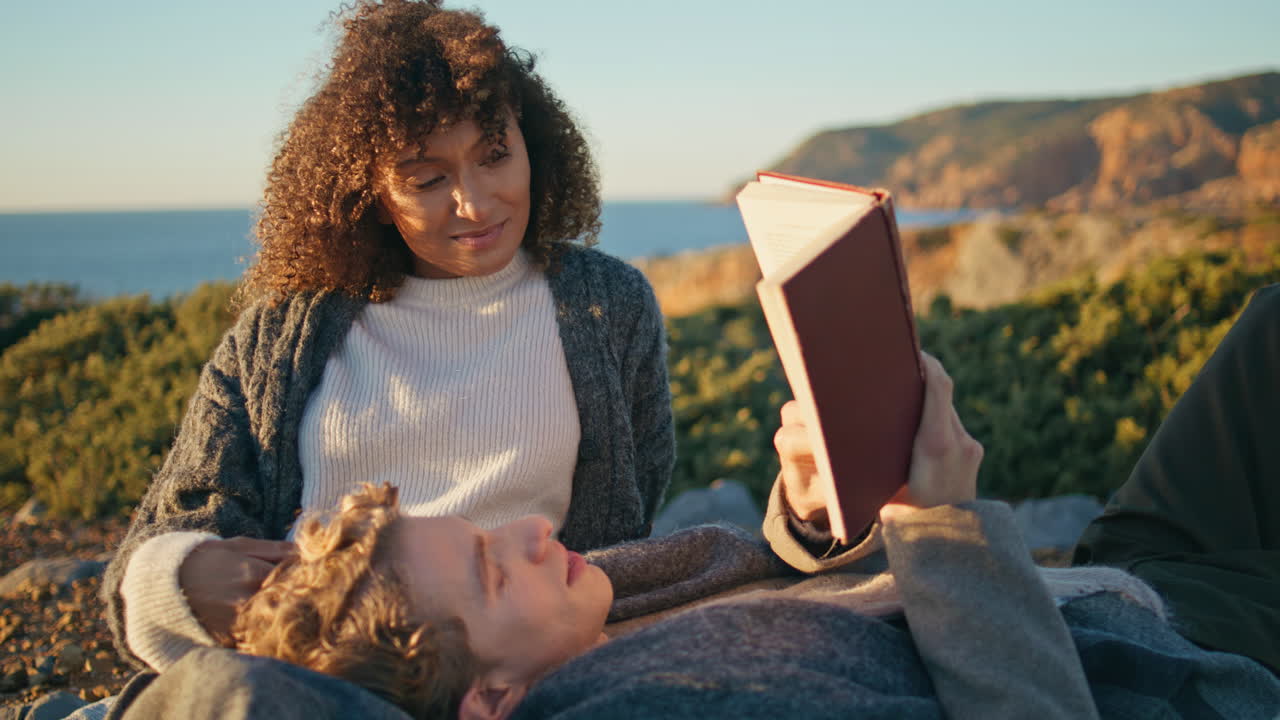 Carefree couple lying cliff with book closeup. Man reading aloud for happy woman
