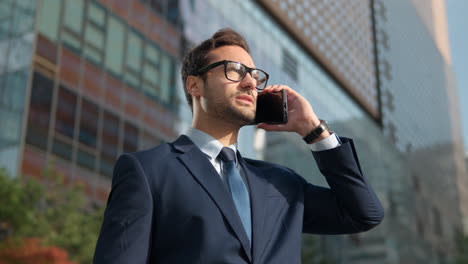 Nahaufnahme-Eines-Lächelnden-Mannes,-Der-Vor-Dem-Bürogebäude-Mit-Dem-Mobiltelefon-Spricht