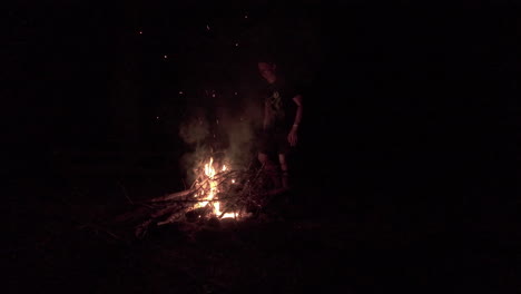 -Shot-of-a-man-standing-and-warming-himself-using-fire-outdoor-during-a-winter-night