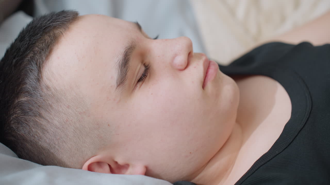Close up of cute kid stretching on bed under blanket opening eyes with warm smile showing relaxed morning wakeup comfort wellness tranquility in cozy bedroom with natural daylight