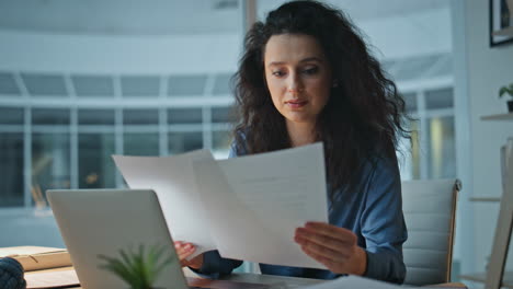 smiling woman analyzing papers in night office. closeup late worker type laptop