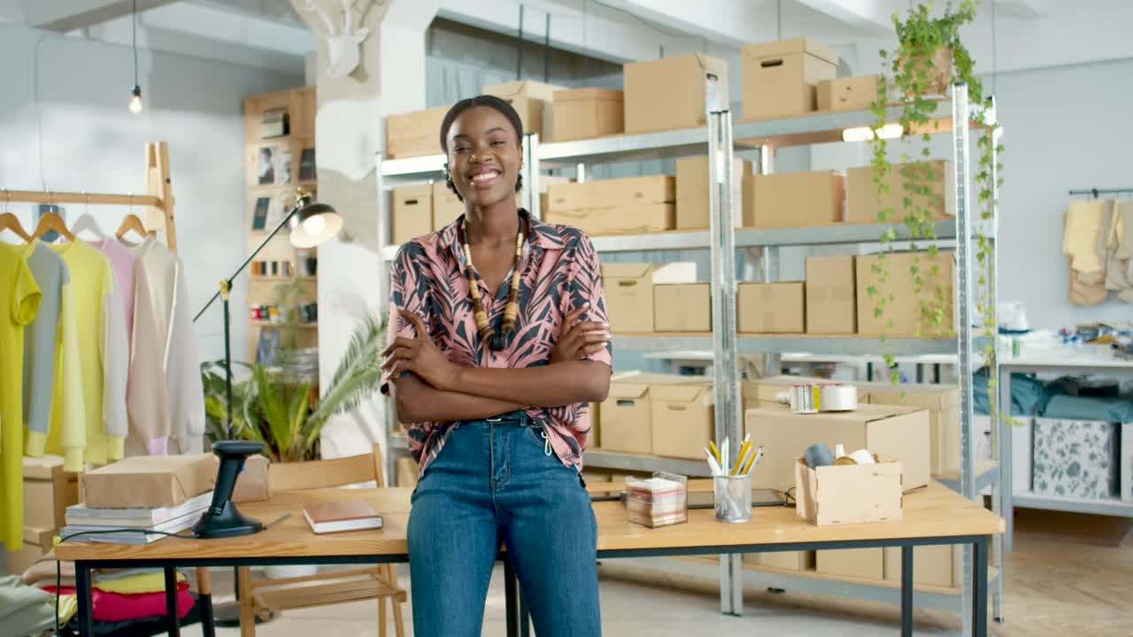 African American woman designer in black mask looking at camera in positive mood in clothing store