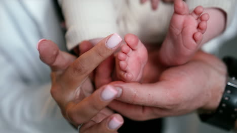 adorable little feet of a newborn in a big male hand. female hand strokes little toes. daddy, mommy and infant baby. close up.