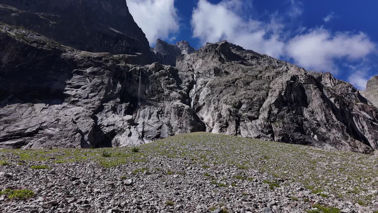 Drone che vola in avanti con la telecamera che si inclina verso l'alto su un campo di rocce, in direzione di una cascata in 4K