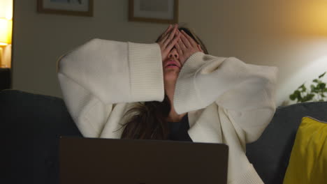 stressed anxious woman spending evening at home sitting on sofa reacting to internet or social media news or financial story on laptop