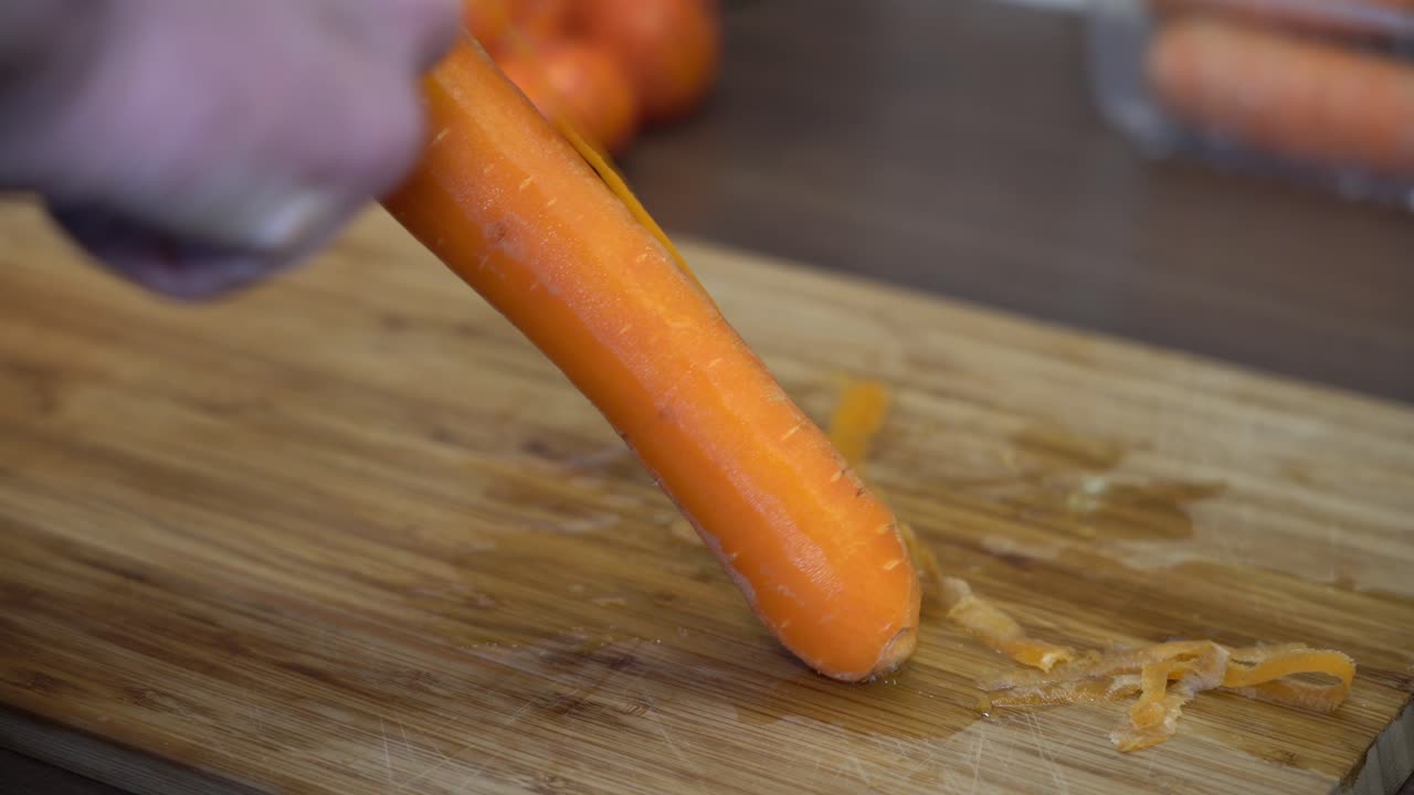 Primo piano di una carota fresca e matura che viene sbucciata - Mano davanti alla carota con la carota a fuoco 24 fps