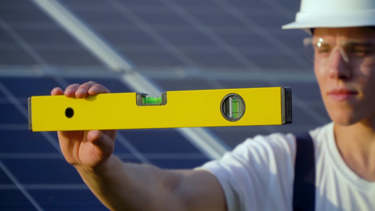 Engineer male inspector in a white helmet check the horizontal level of the solar panel by spirit level. Green energy concept