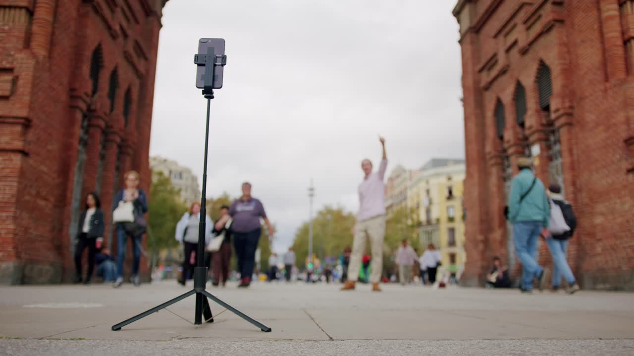 Man blogger making videos using selfie stick phone smartphone taking photo with dance for internet blog on street. Young guy tourist having video call on cellphone walking outdoors in Barcelona spain