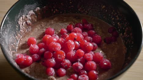 a close up shot of a black dessert bowl filled with a mixture of oatmeal, protein powder and low fat cheese, as tasty frozen red currants are added to the dish creating a low calorie protein pudding