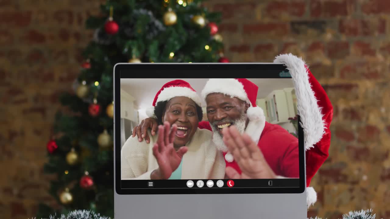 una pareja de ancianos afroamericanos con sombreros de santa en una videollamada en la computadora, con un árbol de navidad
