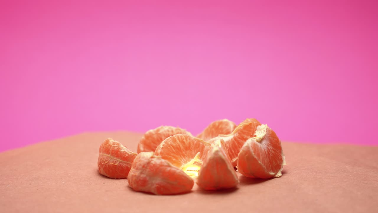 잘 익은 껍질을 벗긴 만다린, 분홍색 및 오래된 종이 배경 4k 비디오에서 색 보정을 사용하여 회전