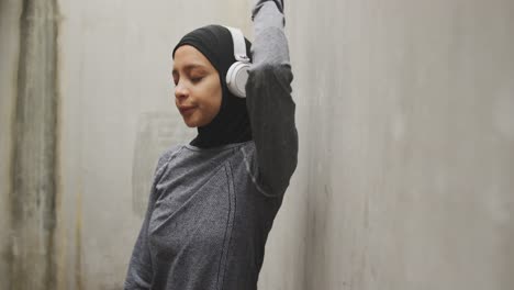 exhausted woman in sportswear with wireless headphones wearing hijab