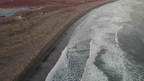 Inclinación-Aérea-Hacia-Arriba-Que-Revela-La-Costa-Islandesa,-Montañas-Cubiertas-De-Nieve-En-El-Fondo