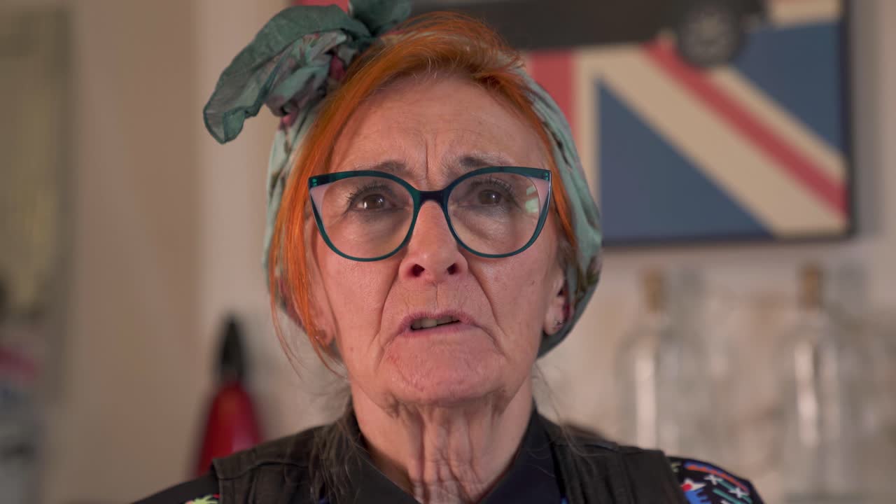 Primo piano di una pensionata che parla durante un'intervista con occhiali eleganti e toni rassicuranti