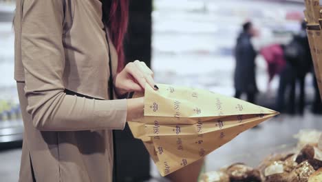 young beautiful red haired woman is picking out backery and putting in into a paper bag. shopping at local grocery store.