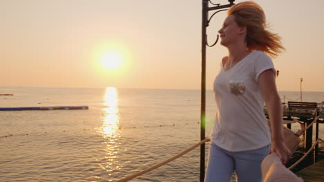 A-Happy-Woman-Is-Walking-Happily-Along-The-Pier-On-The-Seashore-With-A-Hat-In-Her-Hands-Admiring-The