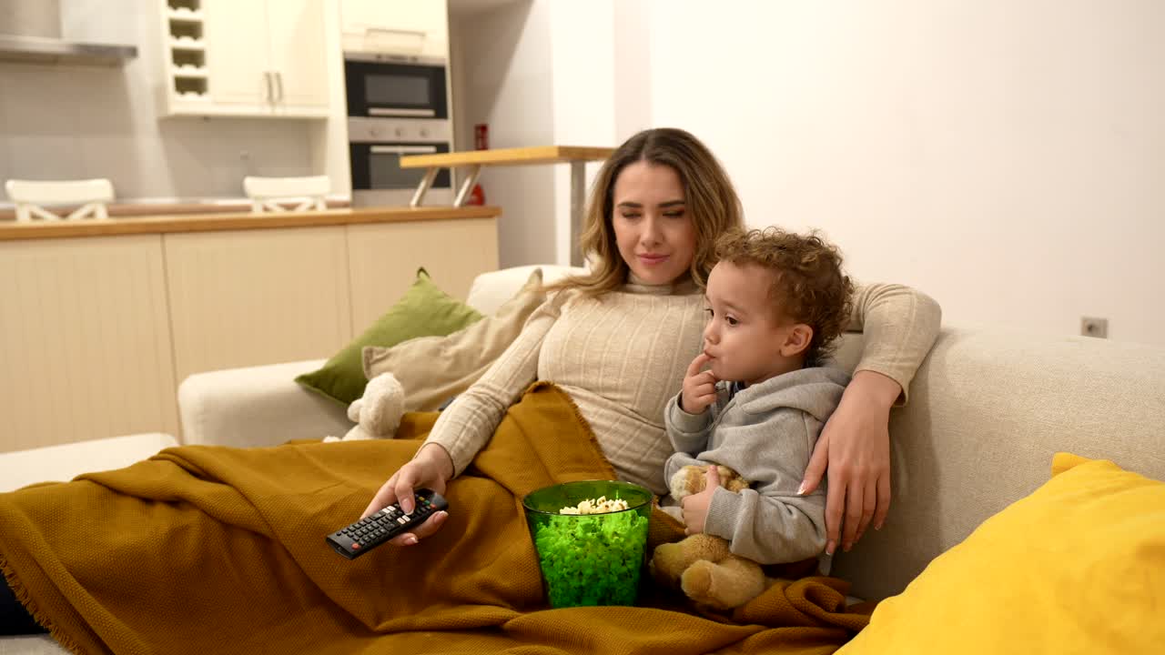 Mor og barn slapper af på sofaen og ser tv og spiser popcorn