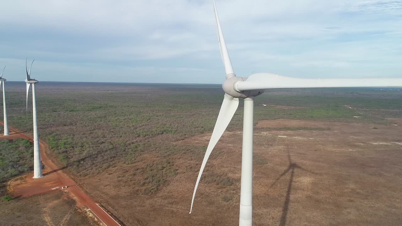 Drone rising very close to a wind turbine, with smooth camera movement, very soft light and machine shadow in the background