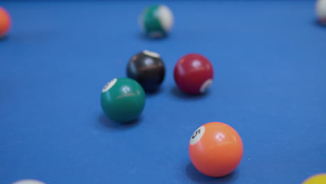 break shot of pool billiard game, triangle of multicolored pocket billiards balls hit with cue ball and scatter on blue table - close-up slow motion