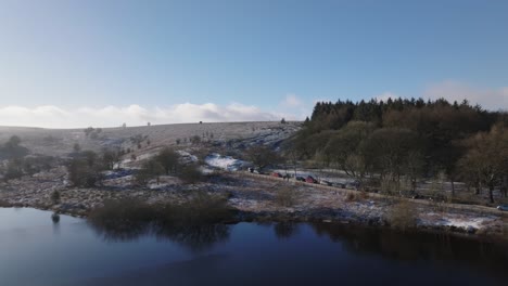 Drone-flight-revealing-winter,-frozen-paths,-trees,-fields-and-a-reservoir-as-some-cars-are-parked-near-the-water