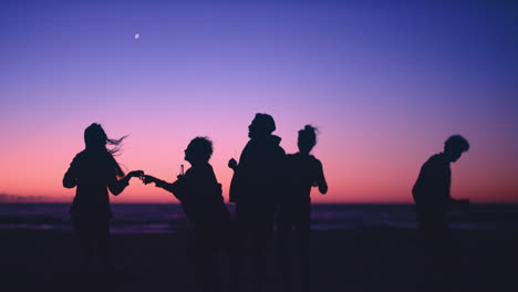 group of friends dancing on the beach at dusk