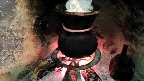 moroccan couscous cooking on a couscoussier steamer to steam it
on a wooden fire in a fireplace, smoke and flame surround the pot-2